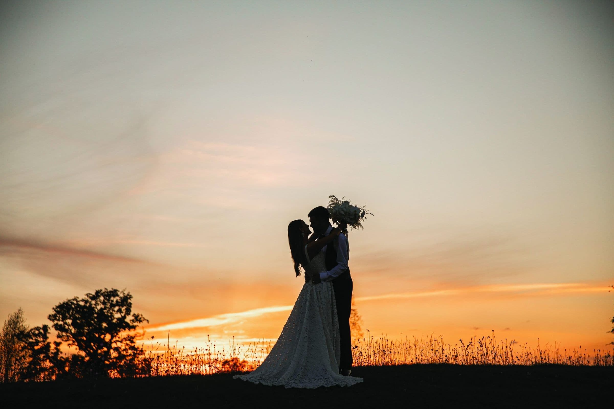 Bride and groom silhouetted against an orange sunset