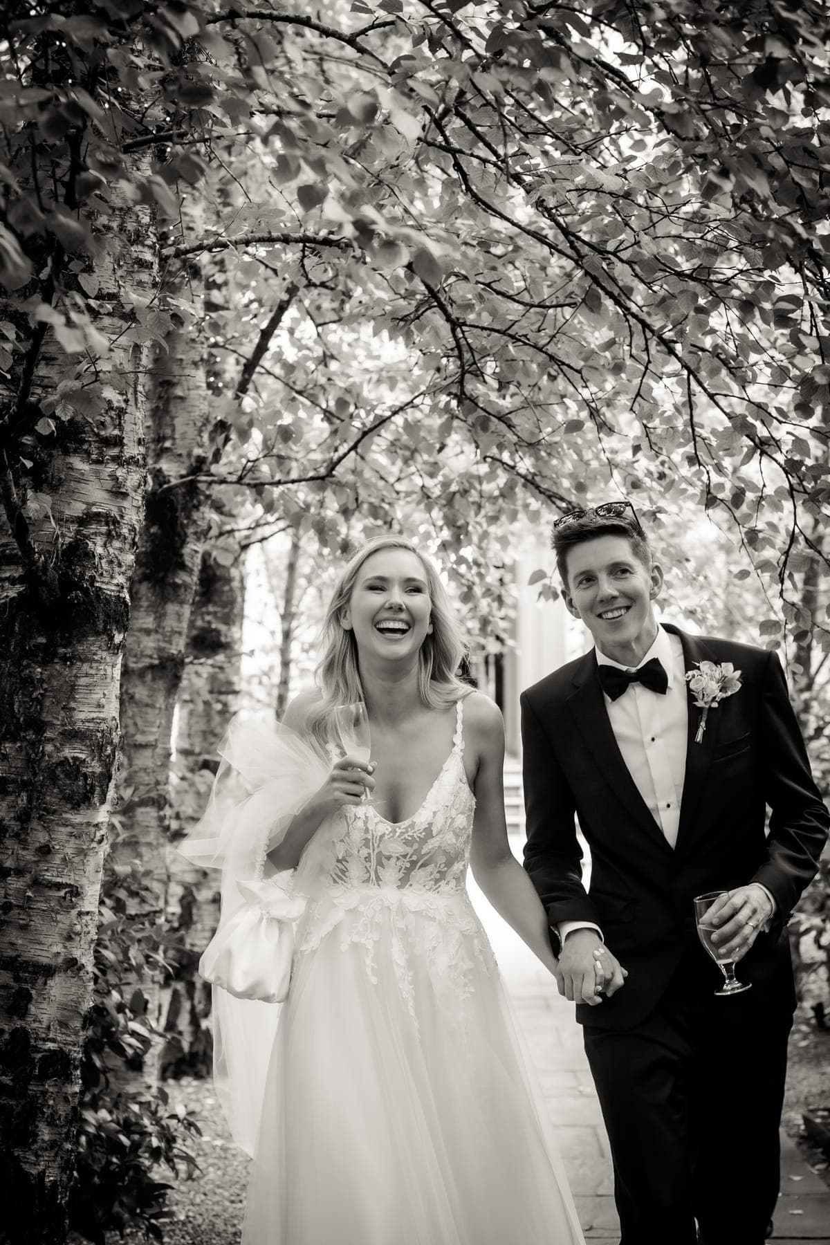 Couple laughing as they walk under the trees, in black and white